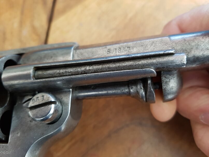 démontage revolver modèle 1873: Dégager l'axe de barillet en tirant la baguette vers l'avant du revolver, puis la faire pivoter